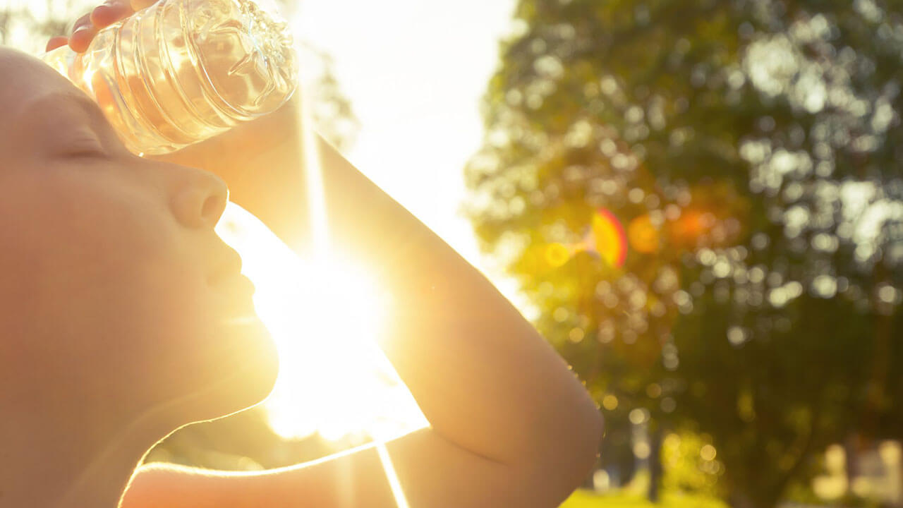 woman outside in the sun holding a water bottle to her forehead
