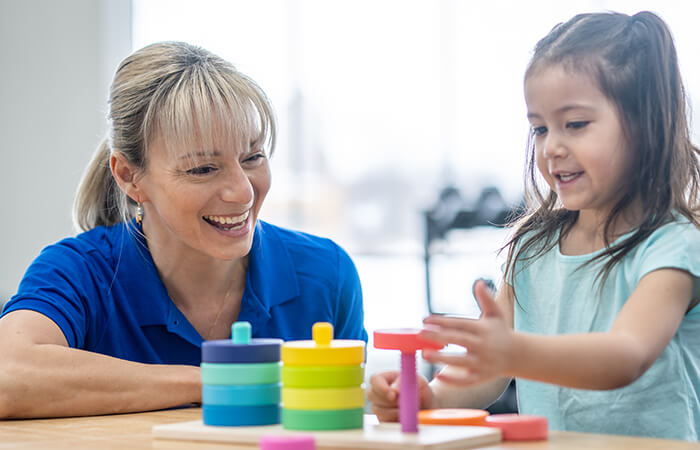 female therapist playing with a stacking game with a young Hispanic child