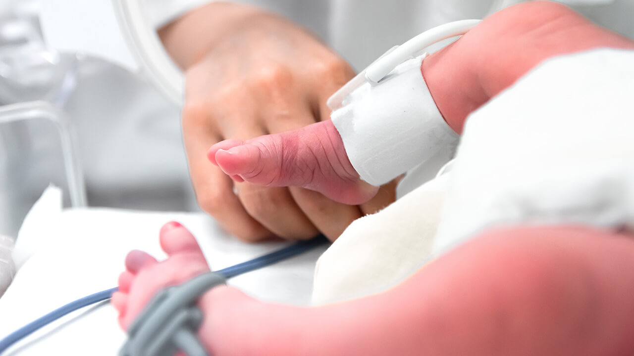 Photo of a doctor holding a baby's foot during an exam in the NICU