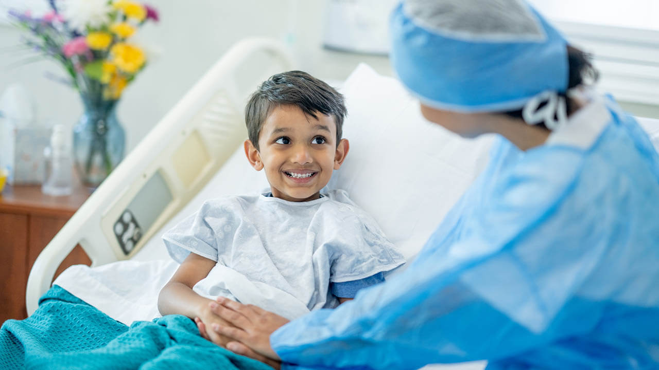Young boy in a hospital bed with surgeon holding his hand