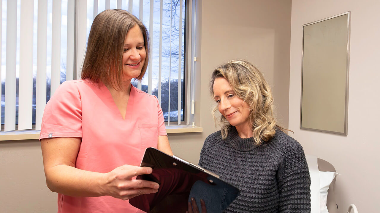 A female doctor wearing pink scrubs is showing a patient their chart