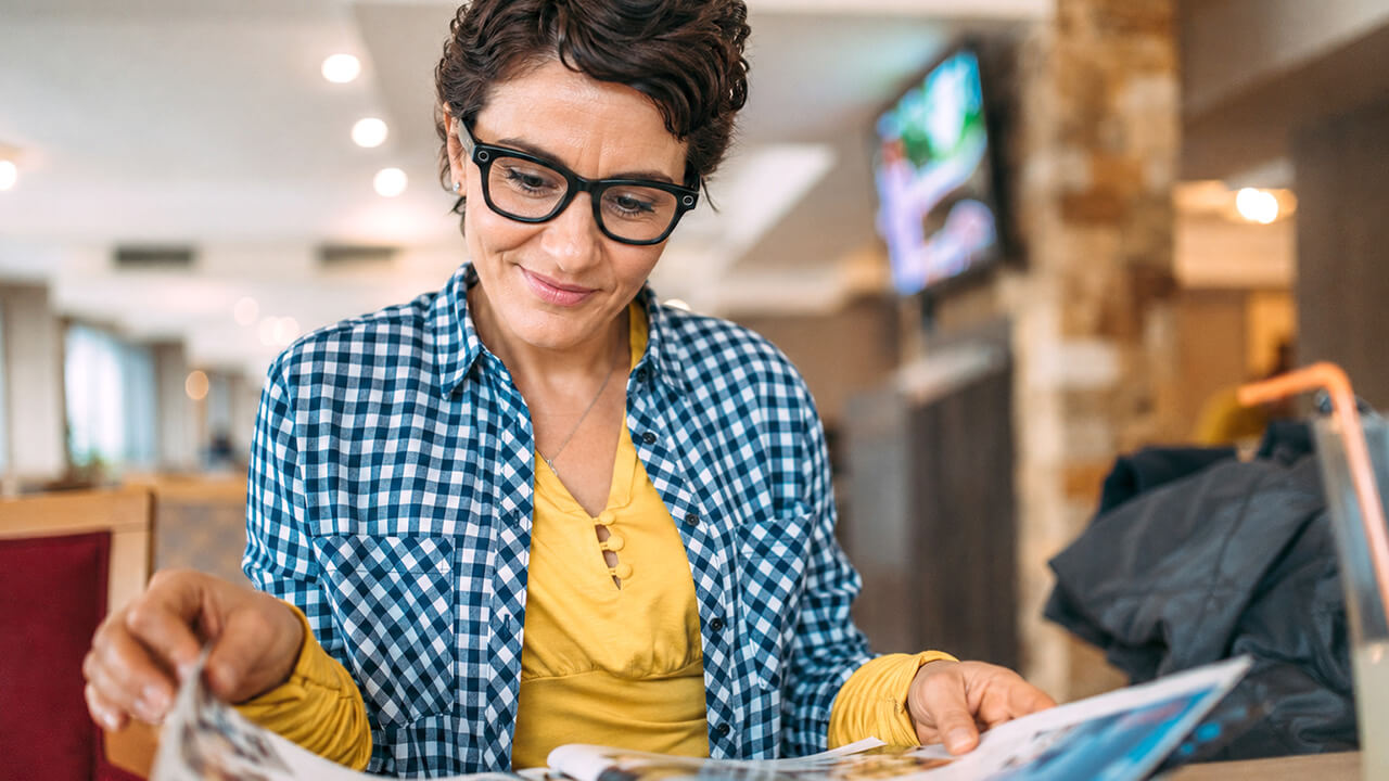 Middle aged woman wearing glasses while looking through a magazine