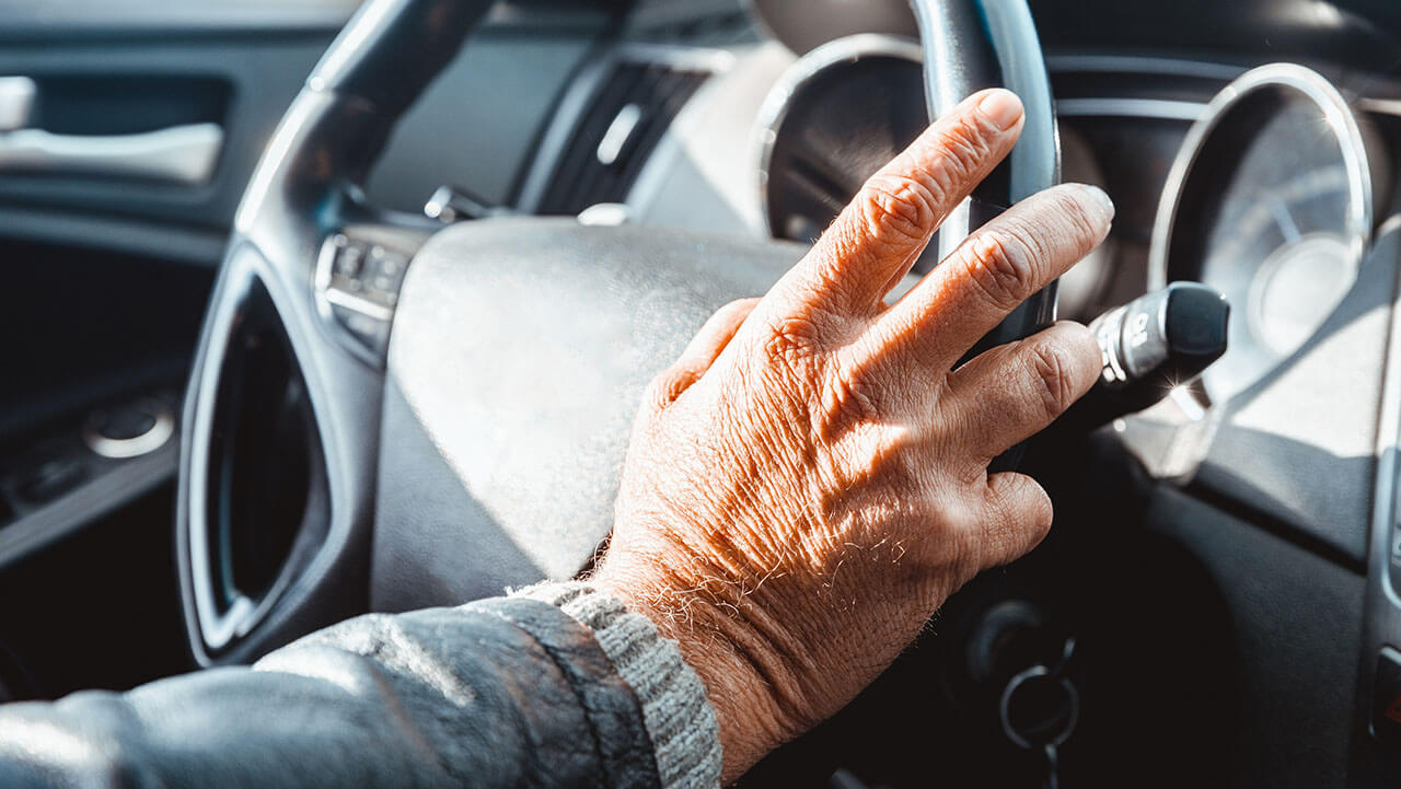 Elderly hand on steering wheel of a car