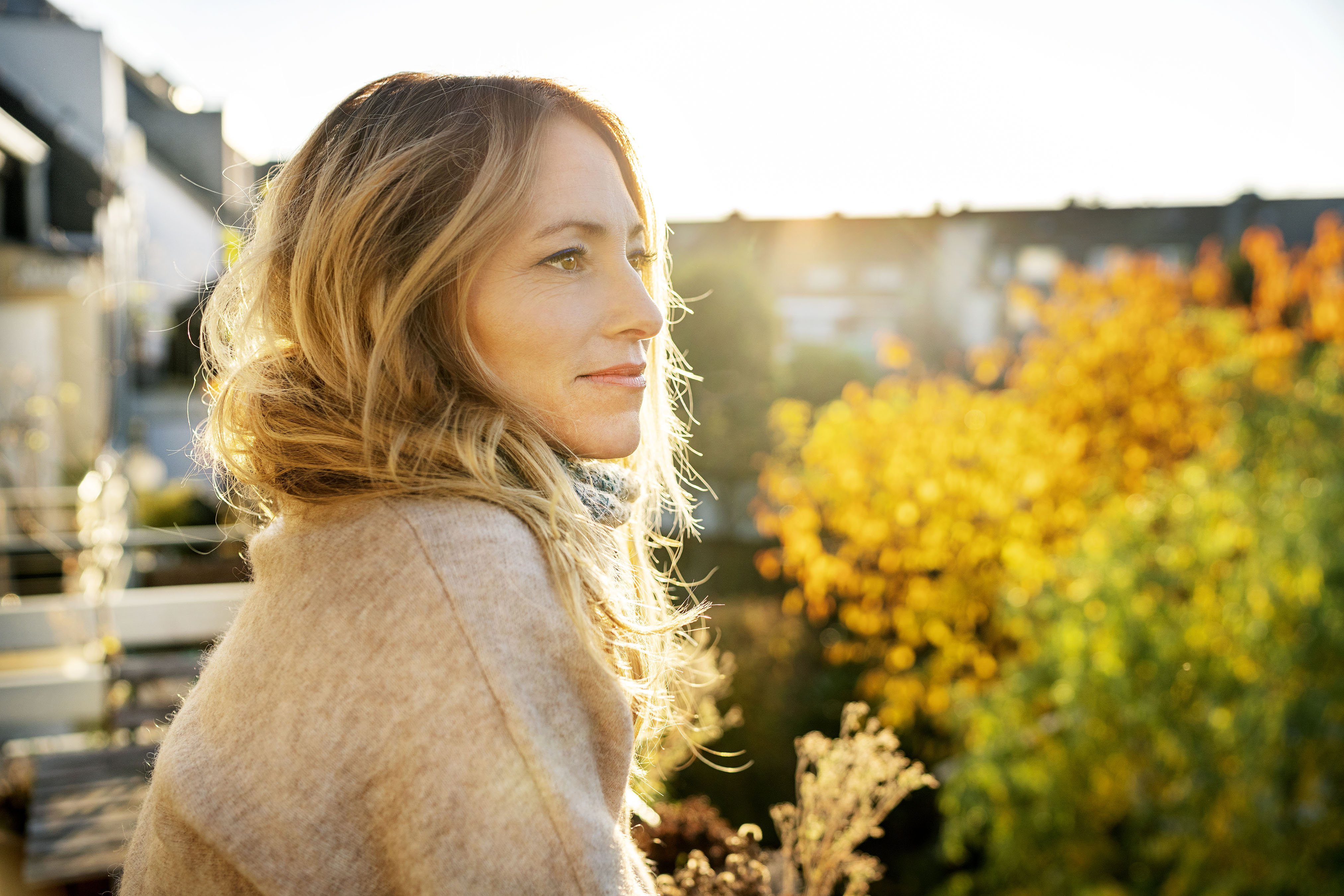 Young woman wearing a red sweater outside with colorful fall leaves behind her