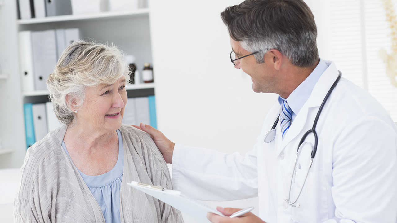 Middle aged male doctor talking to senior woman while holding clipboard