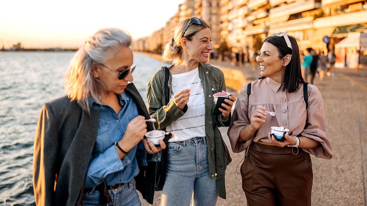 Three women of different ages standing next to a lake and eating ice cream