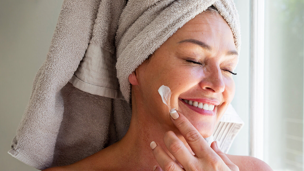 Young woman putting lotion on her face
