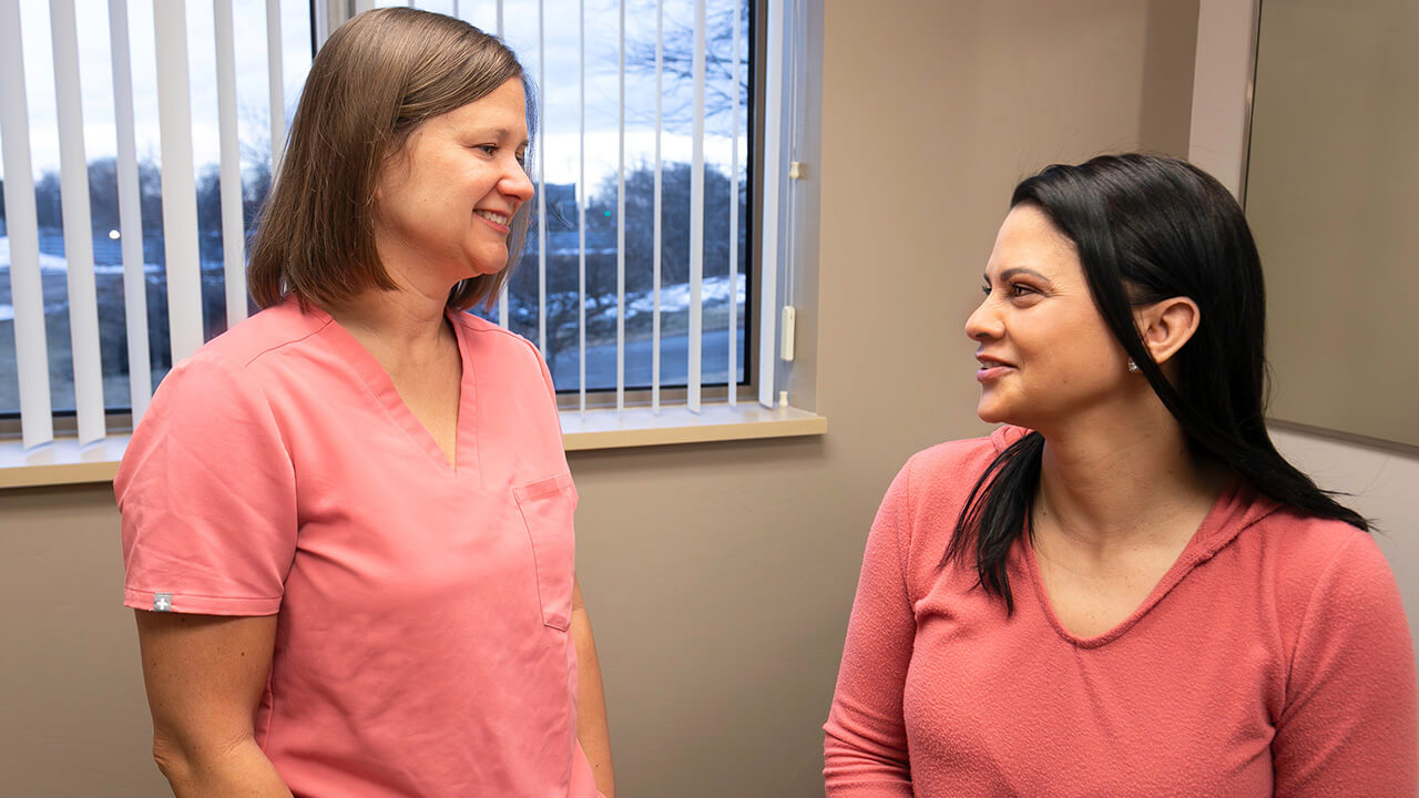 A female doctor wearing pink scrubs is smiling at female wearing a pink outfit