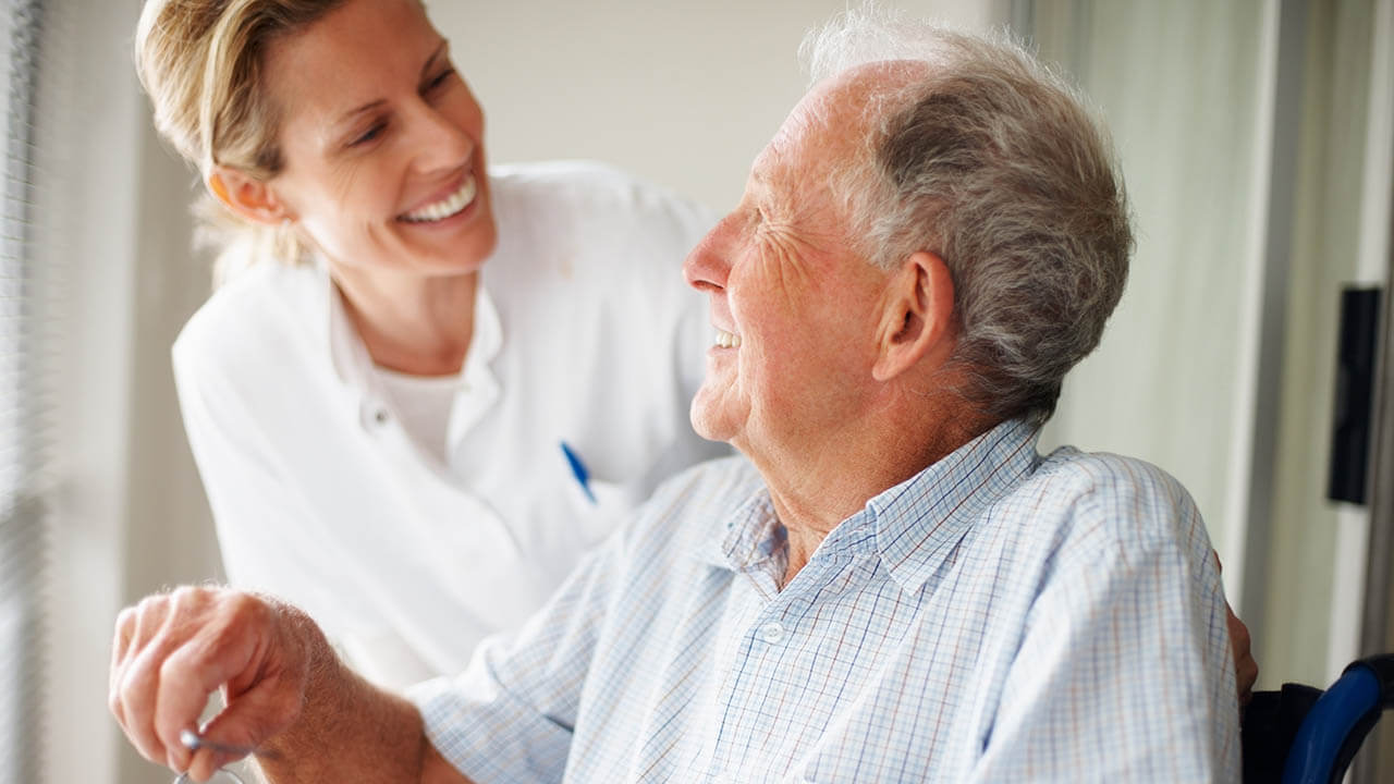 A female doctor leaning over a middle aged man in a wheelchair smiling