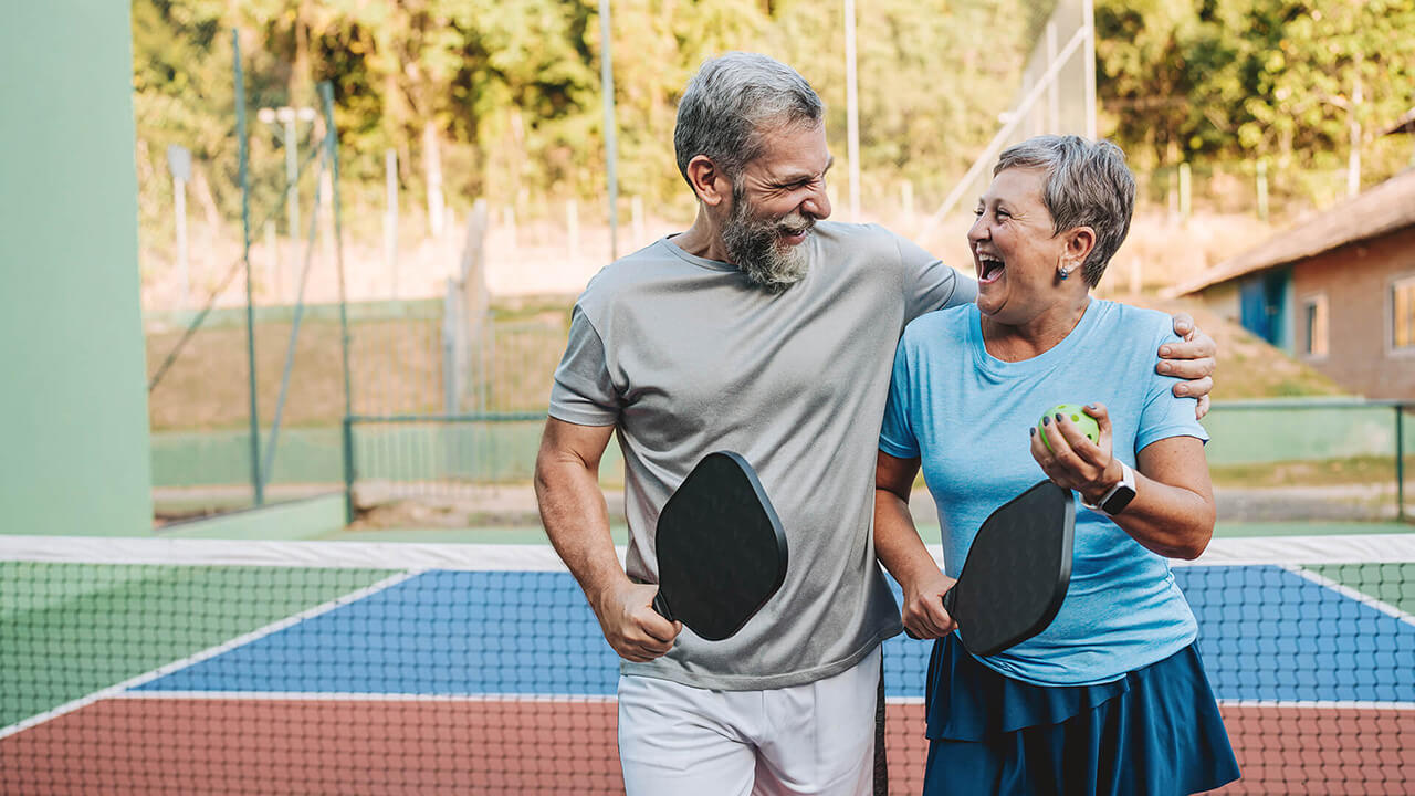 A man and woman smiling while holding pickleball gear