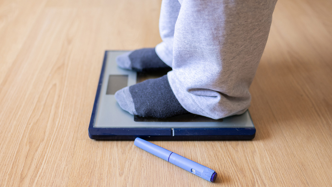 A person standing on a weight scale at home wearing socks and sweatpants