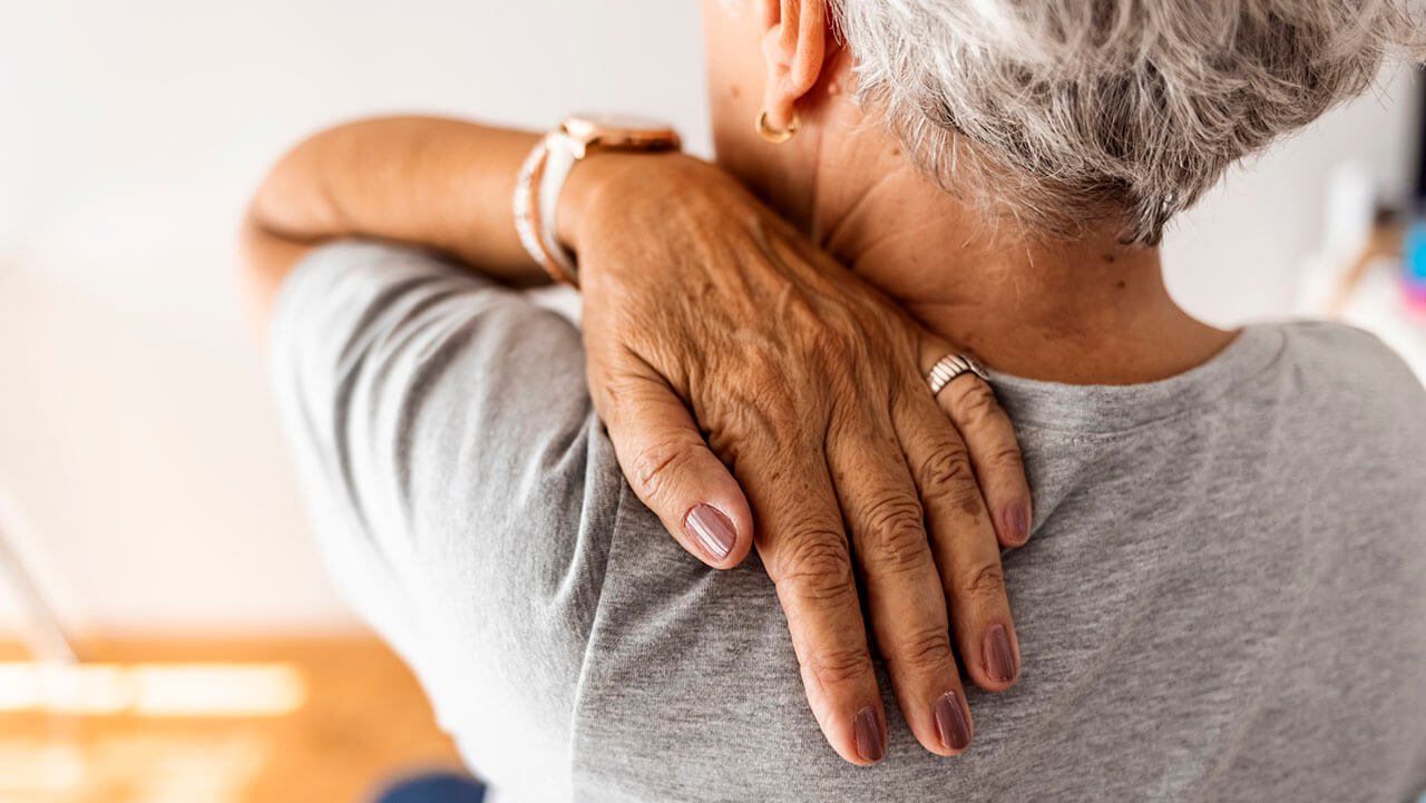 Middle aged woman touching the back of her shoulder
