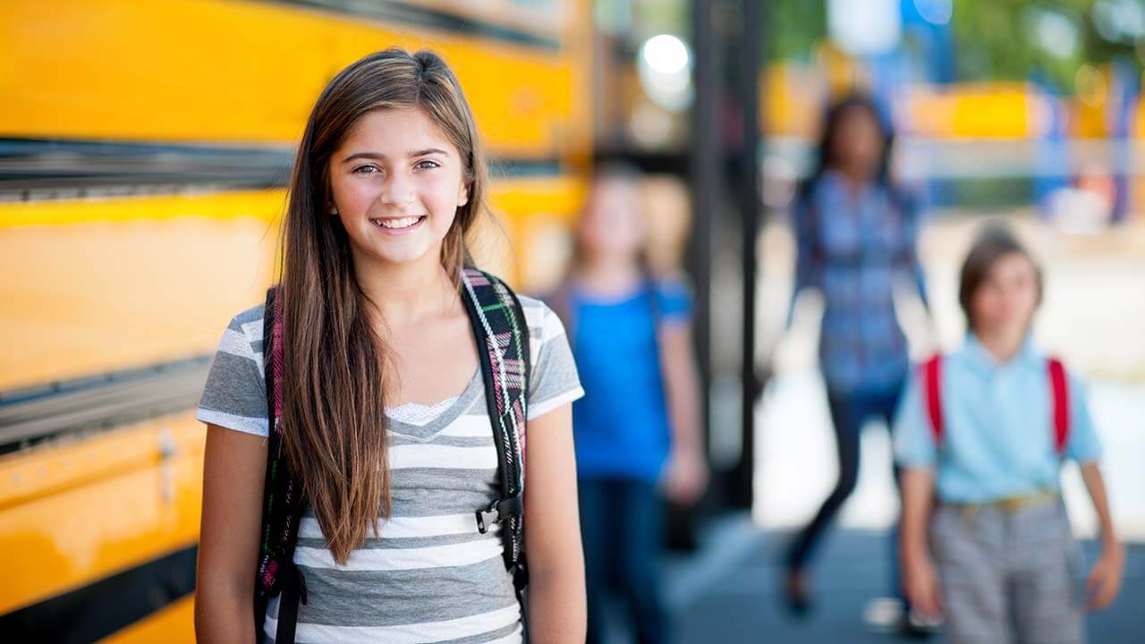 young brunette girl standing in front of a school bus
