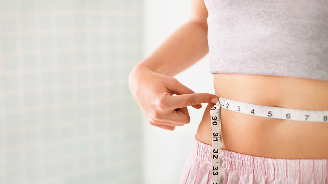 Photo of a female measuring her waist with a tape measure