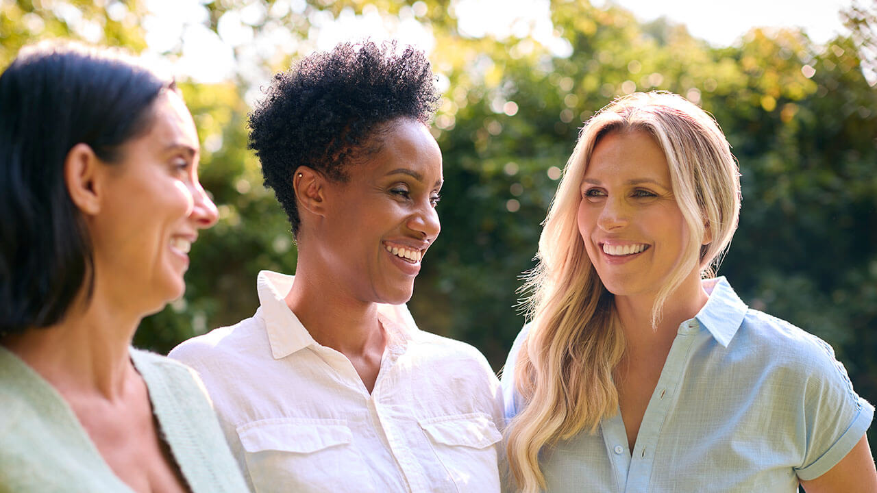 Three women standing together outside and smiling