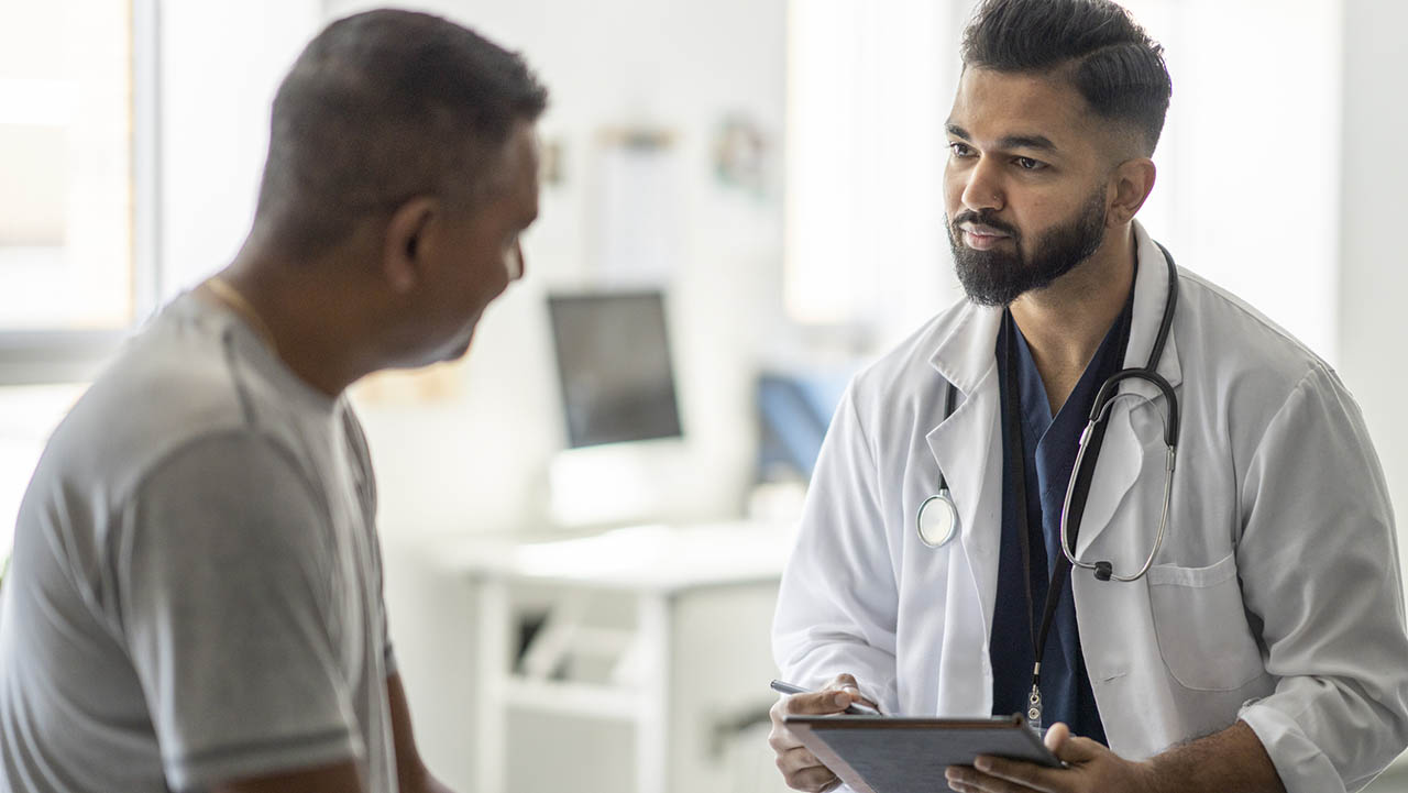Male doctor holding an ipad and talking to a male patient