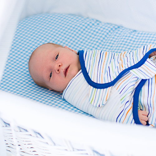 newborn baby laying on back in crib in a swaddle wrap