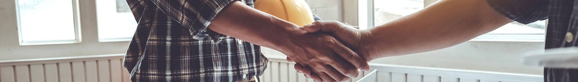 Two contractors shaking hands, one holding a hard hat